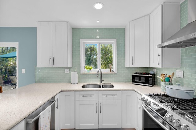 kitchen featuring white cabinets, appliances with stainless steel finishes, sink, and wall chimney range hood