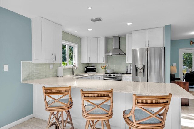 kitchen with wall chimney exhaust hood, a kitchen bar, sink, appliances with stainless steel finishes, and kitchen peninsula