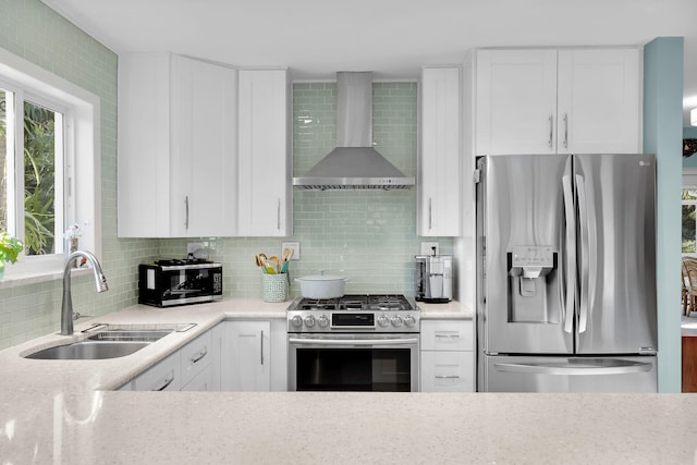 kitchen with stainless steel appliances, white cabinetry, sink, and wall chimney range hood