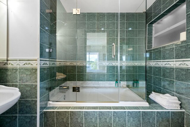 bathroom featuring combined bath / shower with glass door and tile walls