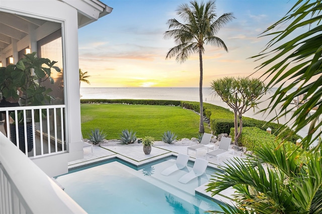 pool at dusk featuring a water view, a patio area, and a yard