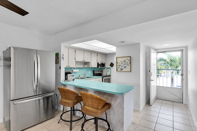 kitchen featuring white cabinetry, appliances with stainless steel finishes, light tile patterned floors, and kitchen peninsula