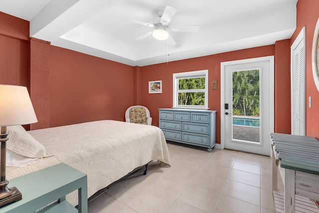 bedroom featuring ceiling fan, a tray ceiling, light tile patterned floors, and access to outside