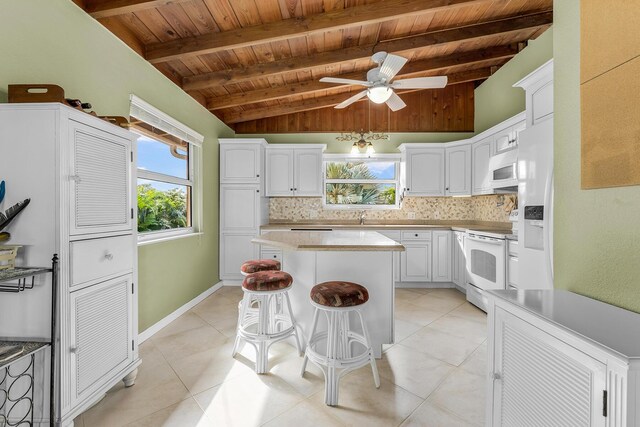 kitchen with light tile patterned flooring, white cabinetry, backsplash, a center island, and white appliances