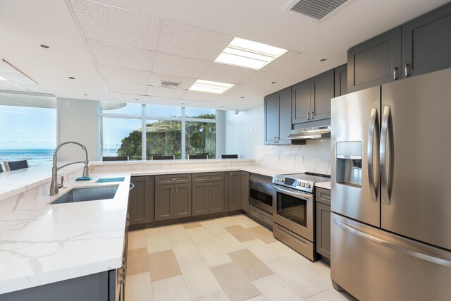 kitchen featuring tasteful backsplash, sink, light stone counters, kitchen peninsula, and stainless steel appliances