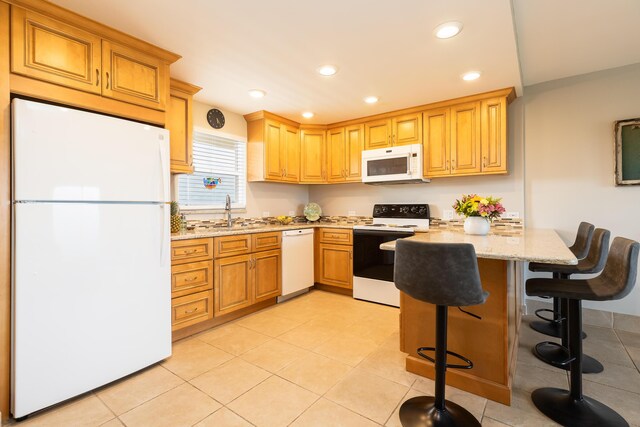 kitchen with a breakfast bar, sink, light tile patterned floors, light stone countertops, and white appliances