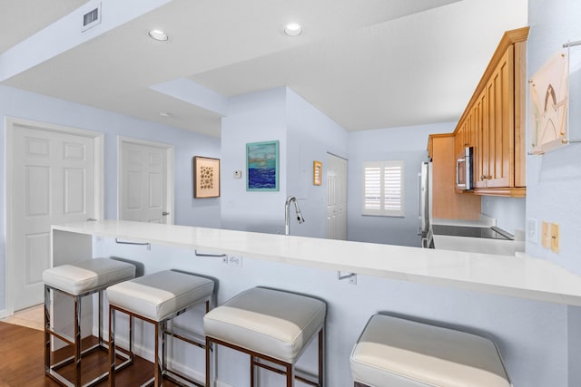 kitchen featuring stainless steel appliances, a kitchen breakfast bar, kitchen peninsula, and hardwood / wood-style floors