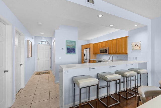 kitchen featuring light tile patterned floors, a breakfast bar area, kitchen peninsula, and appliances with stainless steel finishes