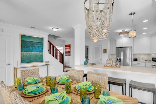 kitchen with hanging light fixtures, decorative columns, stainless steel refrigerator with ice dispenser, ornamental molding, and white cabinets