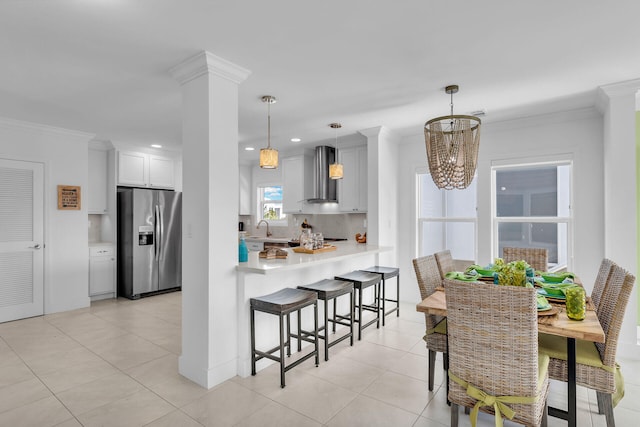 kitchen featuring wall chimney range hood, hanging light fixtures, white cabinets, stainless steel fridge with ice dispenser, and kitchen peninsula