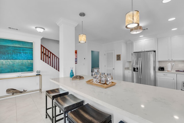 kitchen with light stone counters, stainless steel fridge with ice dispenser, a kitchen breakfast bar, and white cabinets