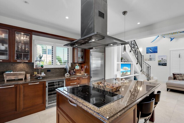 kitchen featuring stainless steel built in refrigerator, island range hood, dark stone countertops, black electric stovetop, and beverage cooler