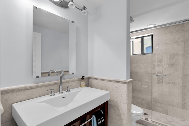 bathroom with vanity, toilet, a shower with shower door, and tile walls