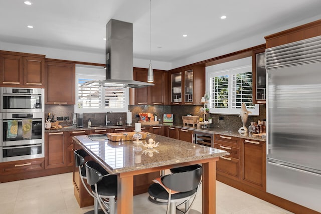 kitchen featuring pendant lighting, a breakfast bar, stainless steel appliances, light stone countertops, and island exhaust hood