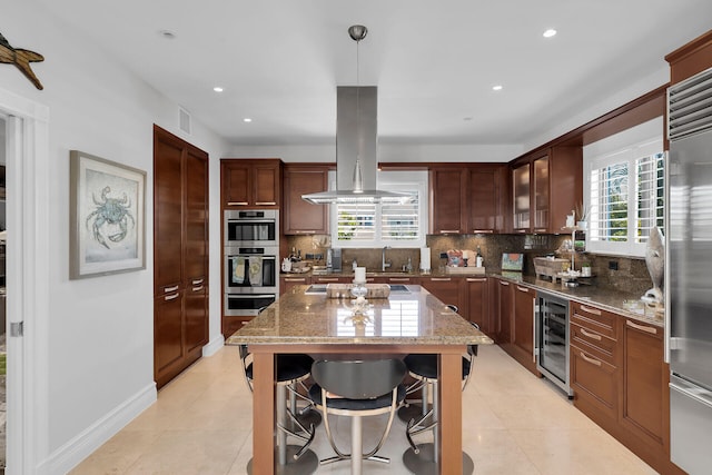 kitchen featuring appliances with stainless steel finishes, island range hood, dark stone countertops, wine cooler, and hanging light fixtures