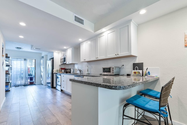 kitchen featuring a kitchen bar, tasteful backsplash, appliances with stainless steel finishes, kitchen peninsula, and white cabinets