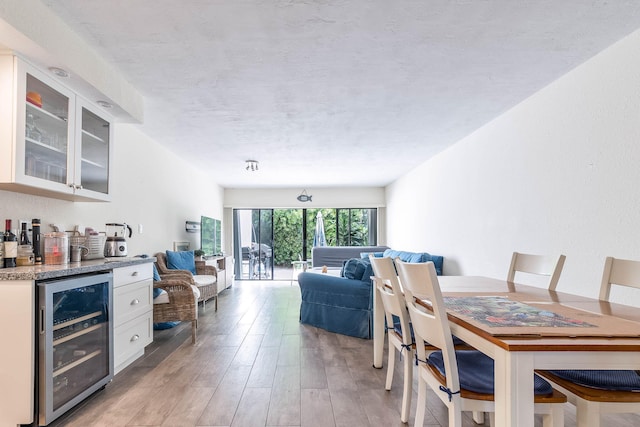 dining room featuring wine cooler, light hardwood / wood-style flooring, a textured ceiling, and indoor bar