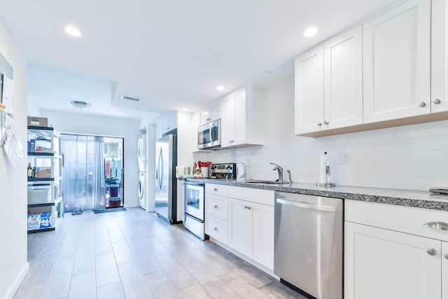 kitchen featuring sink, appliances with stainless steel finishes, white cabinetry, dark stone countertops, and tasteful backsplash