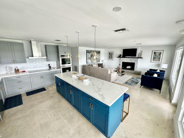 kitchen featuring double oven, tasteful backsplash, a center island, blue cabinetry, and wall chimney exhaust hood