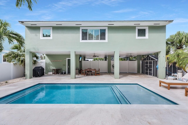 rear view of property with ceiling fan, a storage unit, a fenced in pool, and a patio