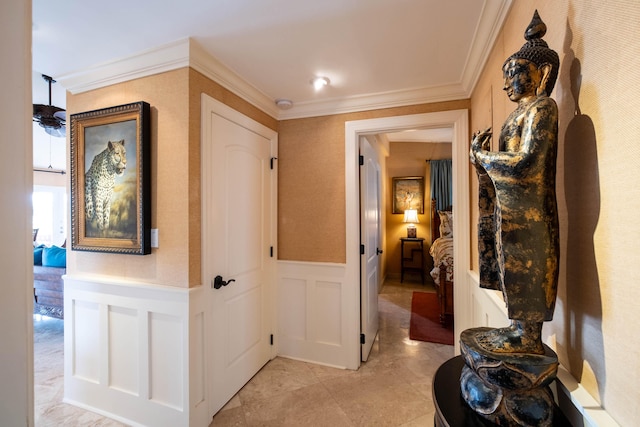 hallway featuring ornamental molding, wainscoting, and a decorative wall