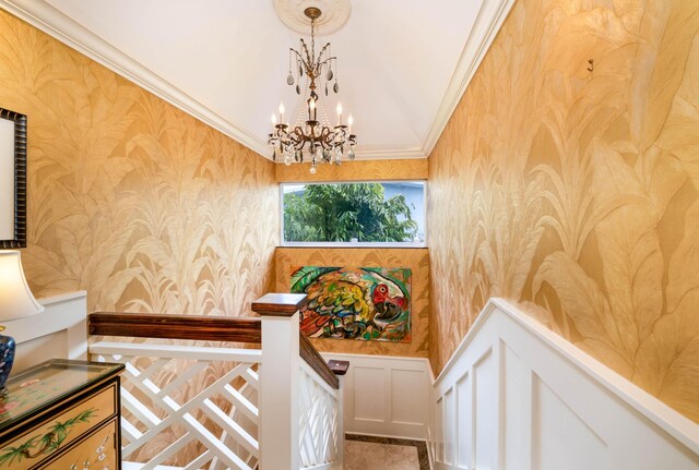 stairway with wallpapered walls, a chandelier, crown molding, and a wainscoted wall