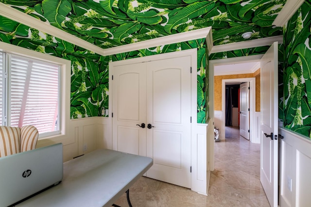 unfurnished office featuring wallpapered walls, crown molding, a decorative wall, and a wainscoted wall