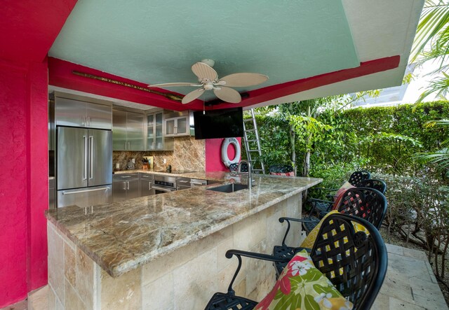 kitchen featuring light stone counters, a peninsula, a sink, appliances with stainless steel finishes, and glass insert cabinets