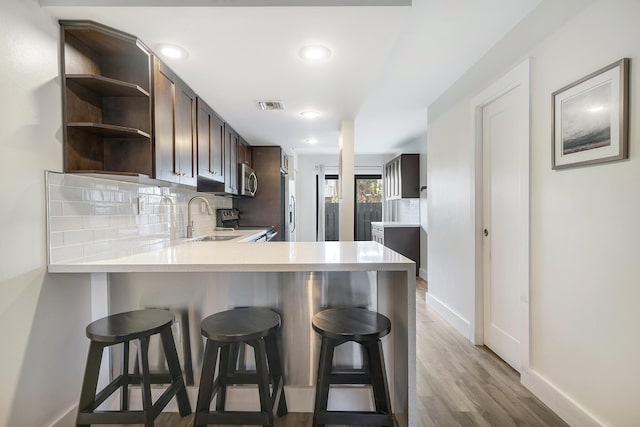 kitchen with a kitchen bar, sink, appliances with stainless steel finishes, kitchen peninsula, and backsplash