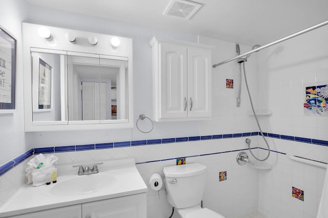 bathroom with tiled shower, vanity, toilet, and tile walls