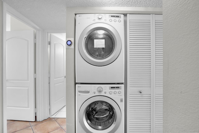 laundry area featuring stacked washing maching and dryer, light tile patterned flooring, and a textured ceiling