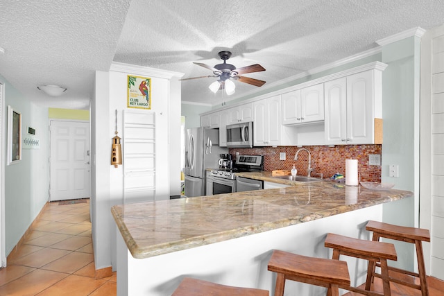 kitchen with appliances with stainless steel finishes, kitchen peninsula, sink, and white cabinets