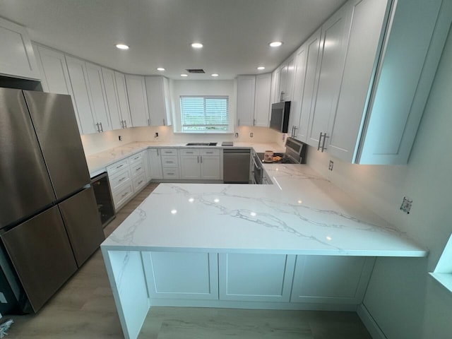 kitchen featuring stainless steel appliances, light stone countertops, white cabinets, and kitchen peninsula