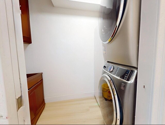 laundry area with cabinets, stacked washer and clothes dryer, and light wood-type flooring