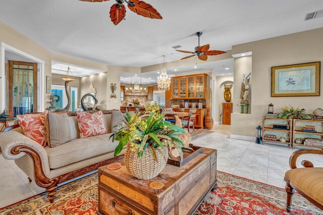 tiled living room with ceiling fan with notable chandelier