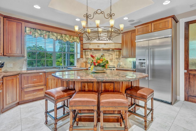 kitchen featuring a kitchen island, stainless steel built in refrigerator, light stone countertops, and a breakfast bar