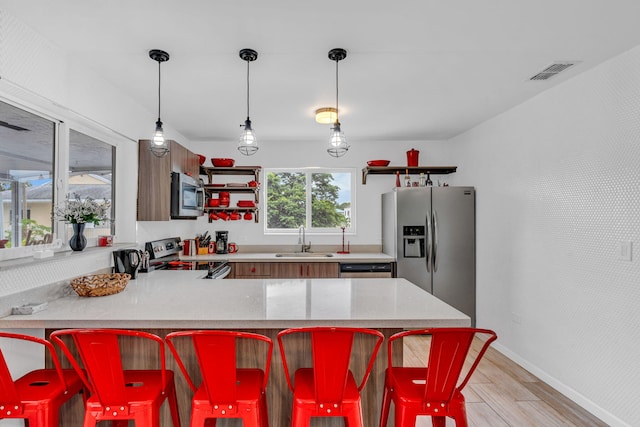 kitchen with sink, light hardwood / wood-style flooring, a breakfast bar area, appliances with stainless steel finishes, and kitchen peninsula