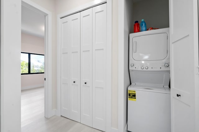 laundry area with stacked washer / drying machine and light wood-type flooring