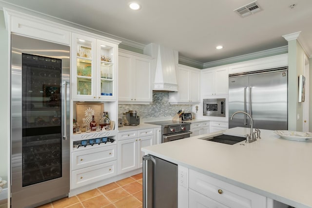 kitchen featuring built in appliances, sink, custom range hood, and white cabinets