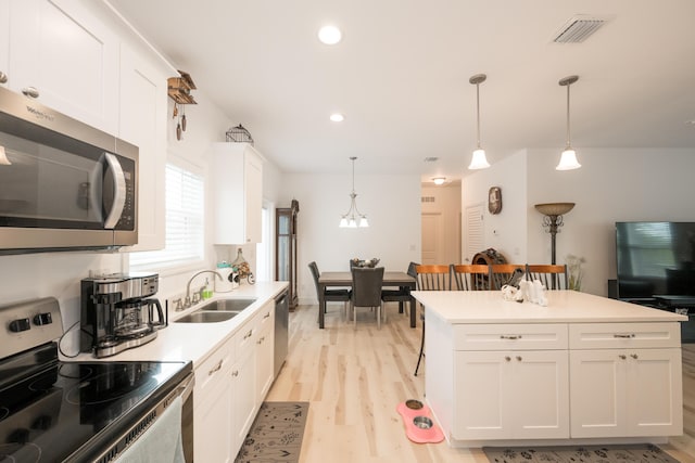 kitchen with appliances with stainless steel finishes, pendant lighting, sink, white cabinets, and light wood-type flooring