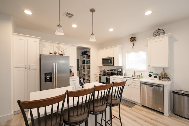 kitchen featuring pendant lighting, sink, white cabinetry, stainless steel appliances, and light wood-type flooring