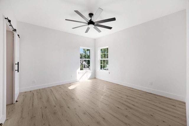 spare room with ceiling fan, a barn door, and light hardwood / wood-style floors