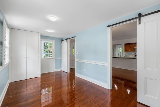 unfurnished room with a barn door and dark wood-type flooring