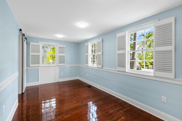 empty room with a barn door and dark hardwood / wood-style flooring