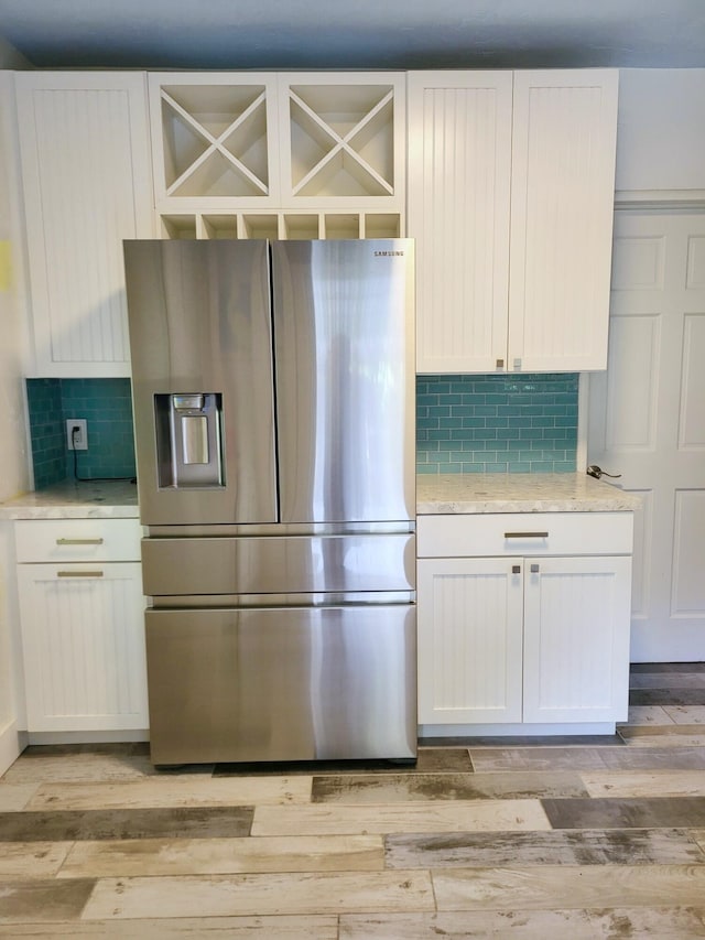 kitchen featuring light wood-type flooring, light stone countertops, stainless steel fridge with ice dispenser, and white cabinets