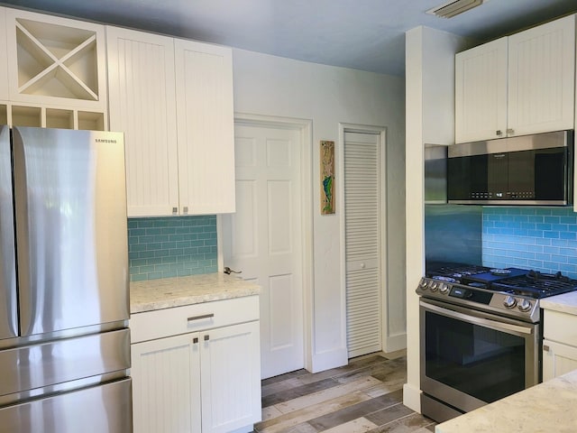 kitchen featuring stainless steel appliances, light stone counters, backsplash, light wood-type flooring, and white cabinetry