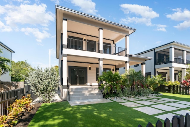 rear view of house with a balcony, fence, a lawn, and french doors