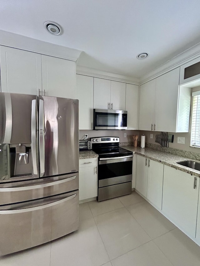 kitchen featuring sink, light tile patterned floors, stainless steel appliances, light stone countertops, and white cabinets