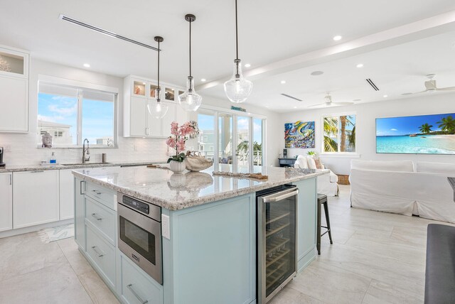 kitchen with sink, stainless steel microwave, white cabinets, a kitchen island, and beverage cooler