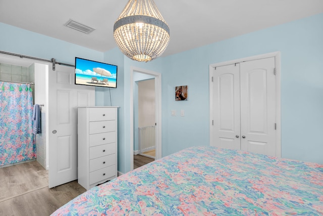 bedroom with a closet, a barn door, light hardwood / wood-style flooring, and a notable chandelier